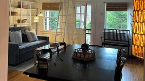 A dining area with a wooden table, chairs, a black sofa, and a ceiling fan.