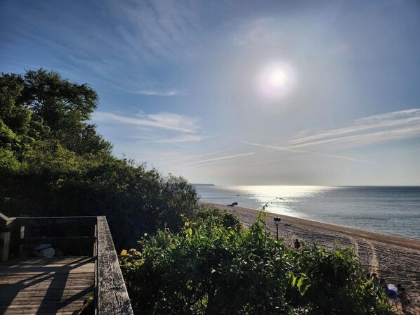 A beach with a wooden walkway leading to a sandy area, surrounded by greenery.