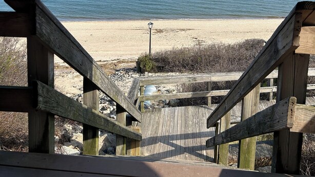 A wooden staircase leading to a beach with a clear view of the ocean.