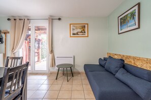 Sala de estar com sofá, mesa e cadeira. Uma porta dá acesso a uma área externa.