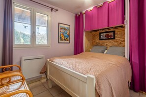 Une chambre  à coucher avec un lit, une fenêtre, un radiateur, une chaise et un mur en bois orné d’un tableau.