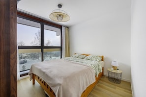 Een slaapkamer met een groot raam, een bed, een nachtkastje met een lamp en een hanglamp.