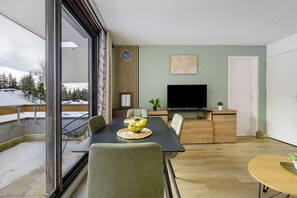 Een moderne woonkamer met een eethoek, een televisie en uitzicht op een besneeerd landschap.