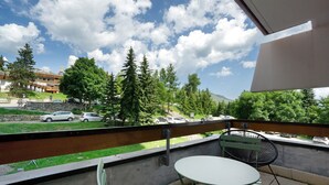 A balcony with a table and chairs, overlooking a parking area and greenery.