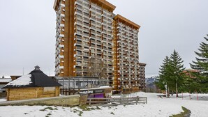 A high-rise building with multiple balconies, a wooden facade, and a small adjacent structure with signage.