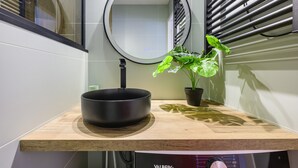 A bathroom with a round mirror, a black basin, a potted plant, and a Valberg brand appliance.