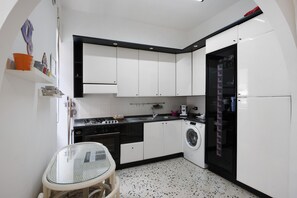 Une cuisine compacte avec des meubles blancs, un lave-linge et une table en verre.