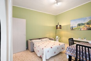 Una stanza con un letto, un tavolo con sedie, una lampada e un quadro appeso al muro.