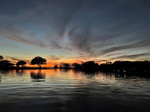 Un lago tranquilo al atardecer, con siluetas de árboles y un cielo despejado.