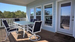 A covered patio with a table and chairs, large windows, and a door with a welcome mat.