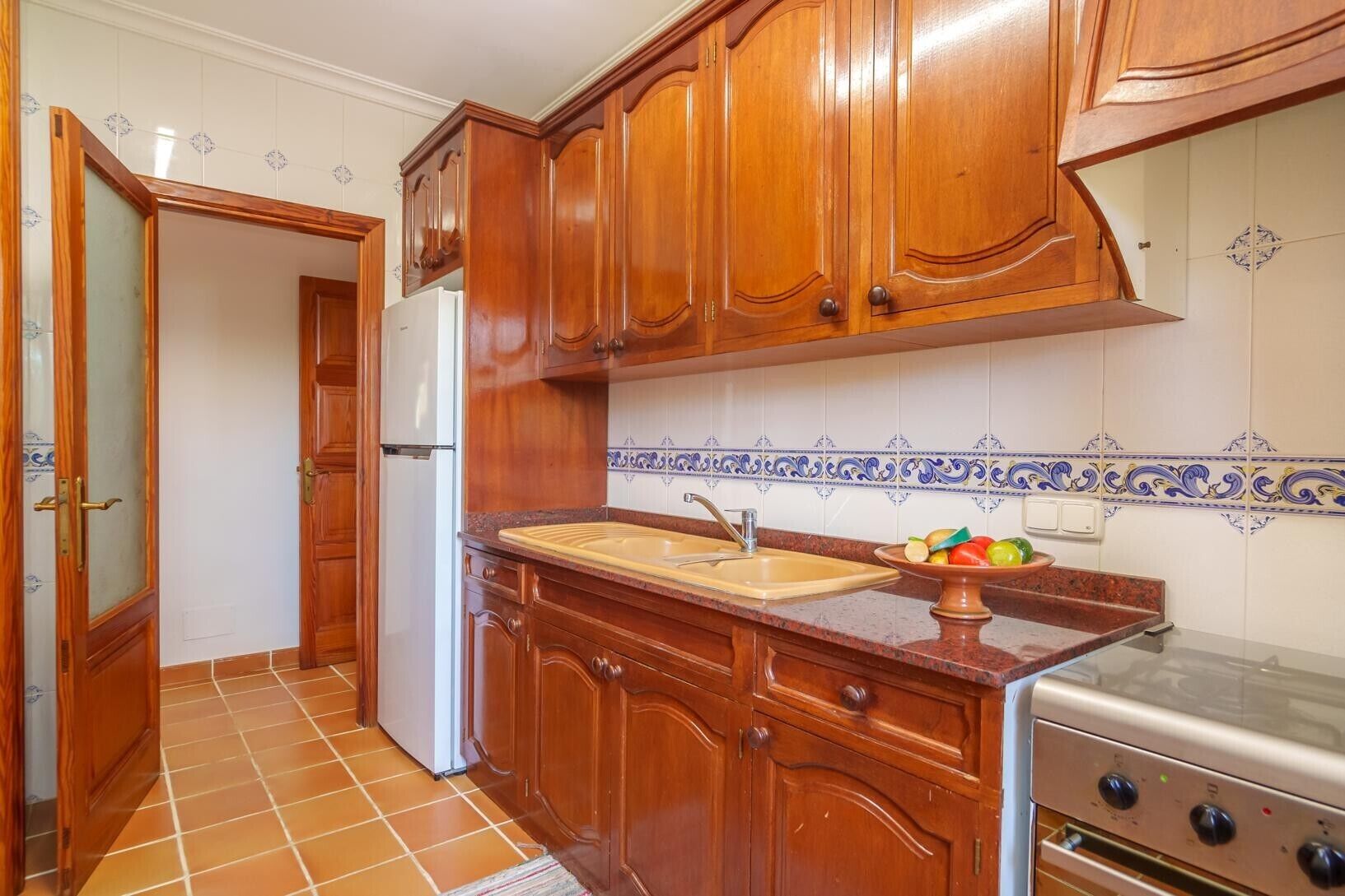 Une cuisine avec des meubles de rangement en bois, un évier, une cuisinière et un réfrigérateur.