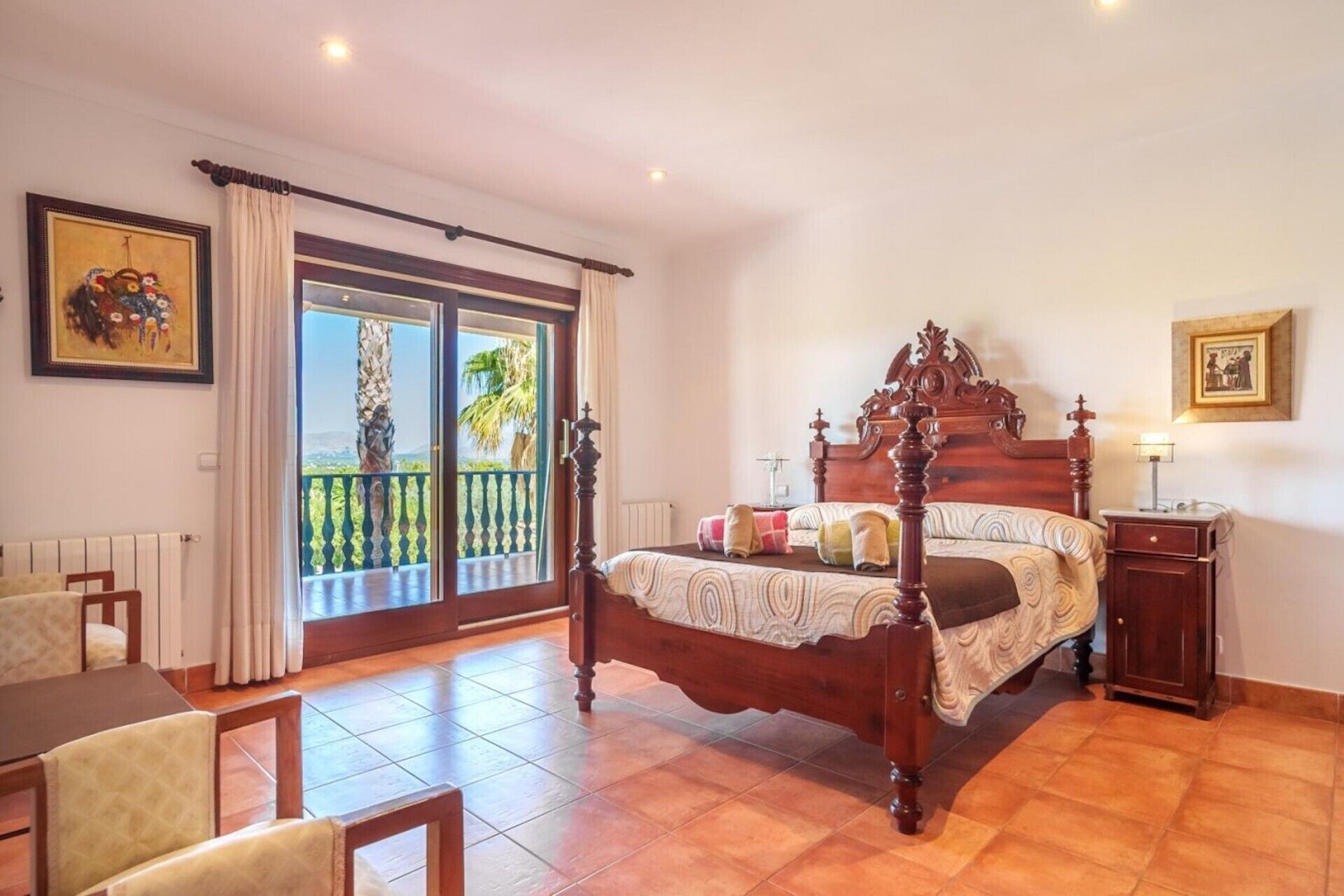 Ein Schlafzimmer mit Himmelbett, einem Balkon mit Aussicht und einer Essecke mit Stühlen.
