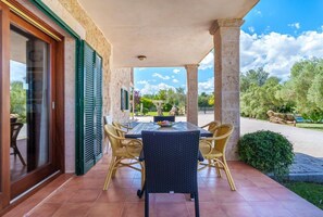 Une terrasse couverte avec une table et des chaises, un mur en pierre et une vue sur le jardin.