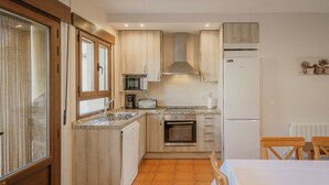 A compact kitchen with wooden cabinets, a built-in oven, a microwave, and a refrigerator. - Tradition Rural El Tío Ricardo Country House – Private Pool & Garden in Segovia (NIEVA)