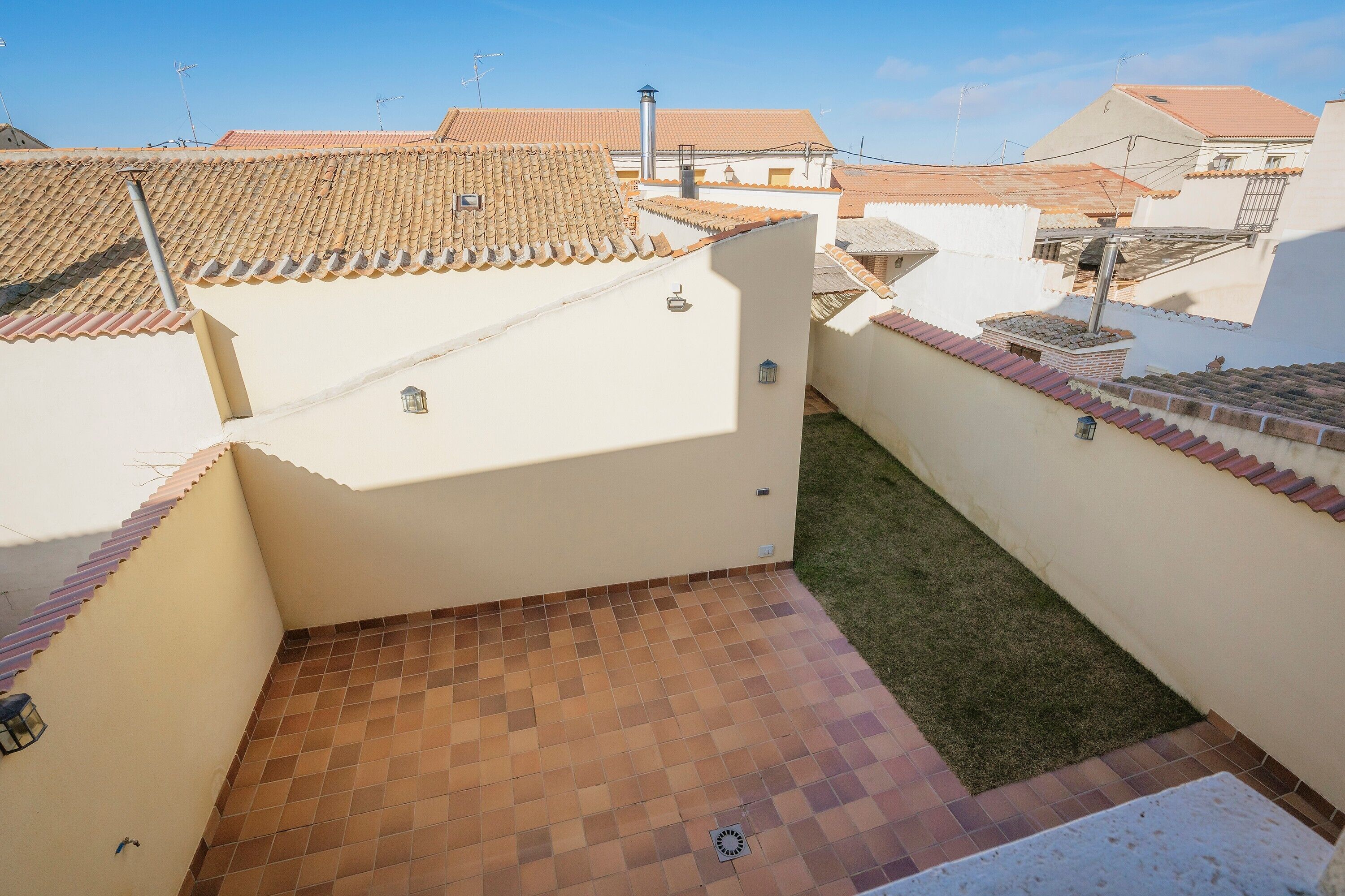Une terrasse sur le toit avec un sol à carreaux, un petit jardin et des bâtiments adjacents présentant une architecture similaire.