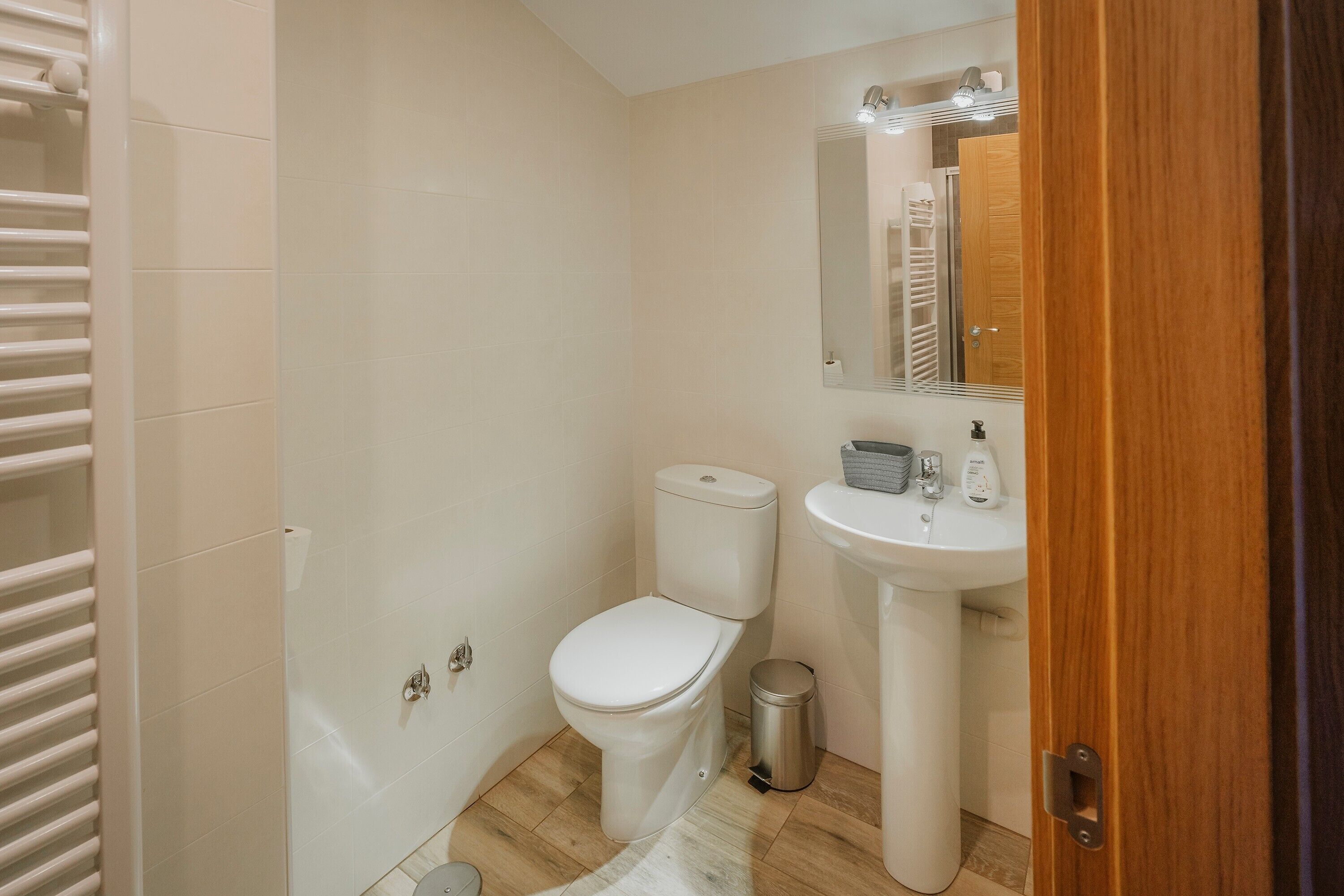Een badkamer met toilet, wastafel, spiegel en een prullenbak.