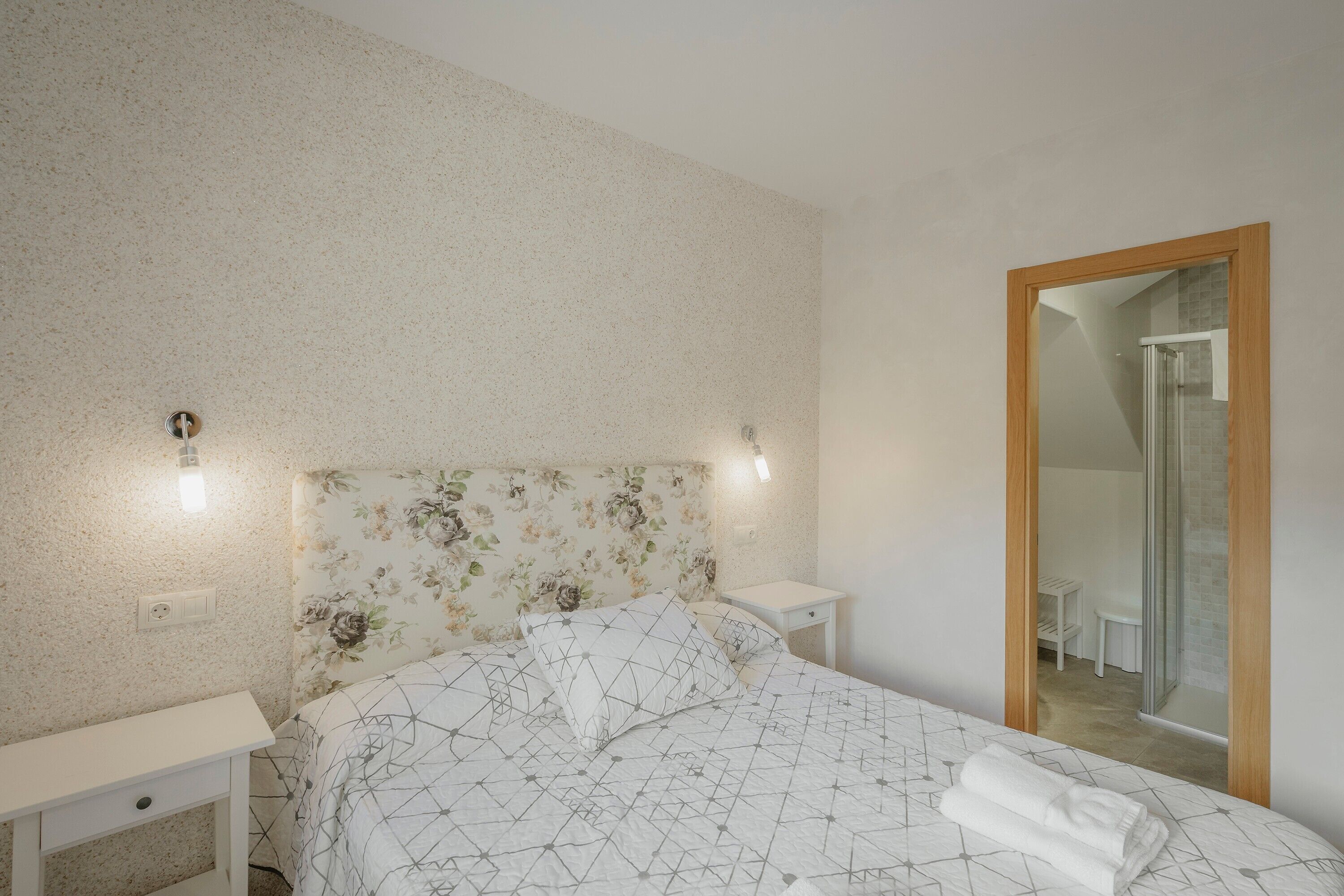 Une chambre à coucher comprenant un lit, des tables de chevet, un miroir et un espace douche.