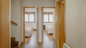 A corridor leading to two bedrooms with wooden doors, a radiator, and a chair. - Tradition Rural El Tío Ricardo Country House – Private Pool & Garden in Segovia (NIEVA)