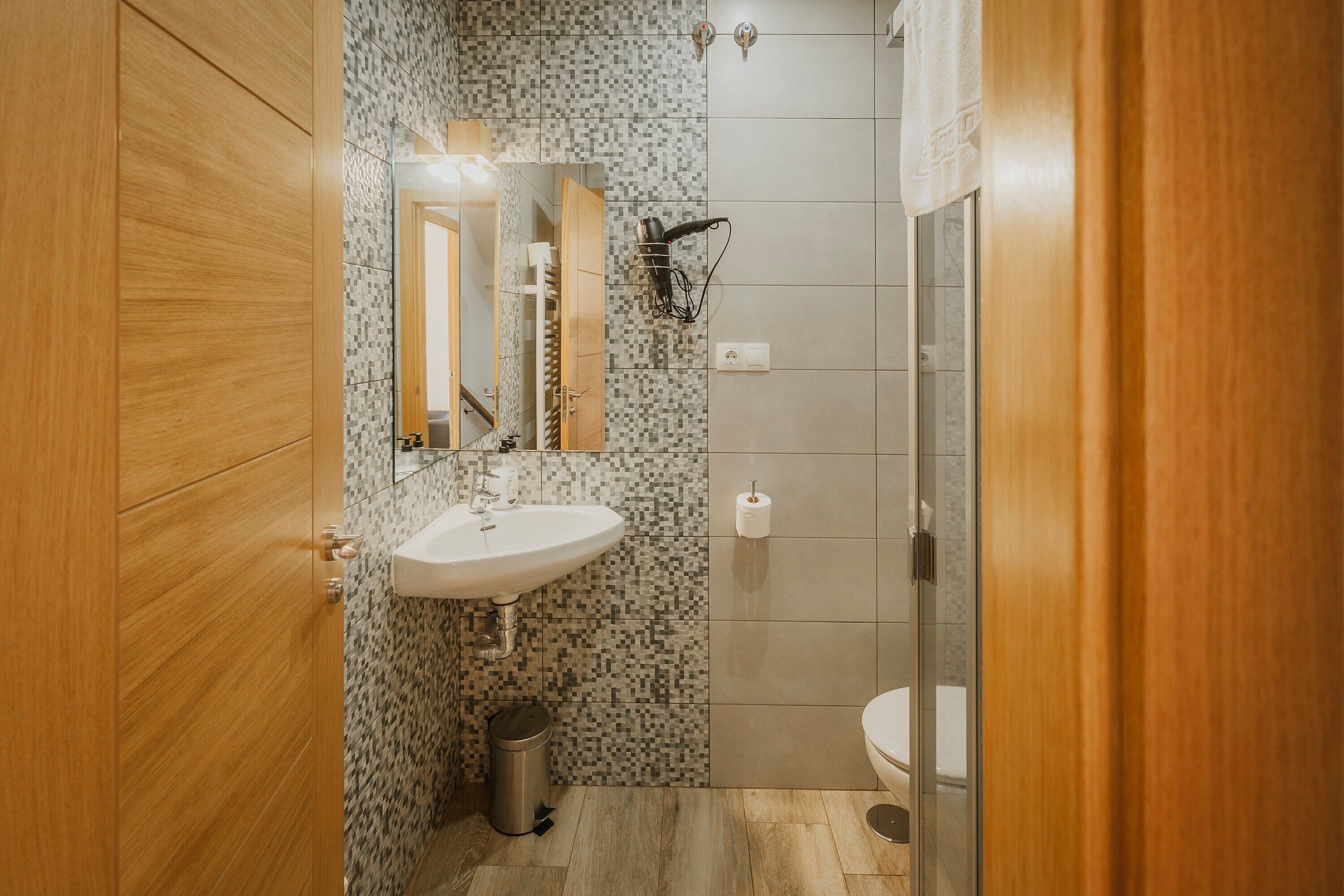 Une salle de bain avec une porte en bois, un lavabo, un miroir, une douche et des toilettes.