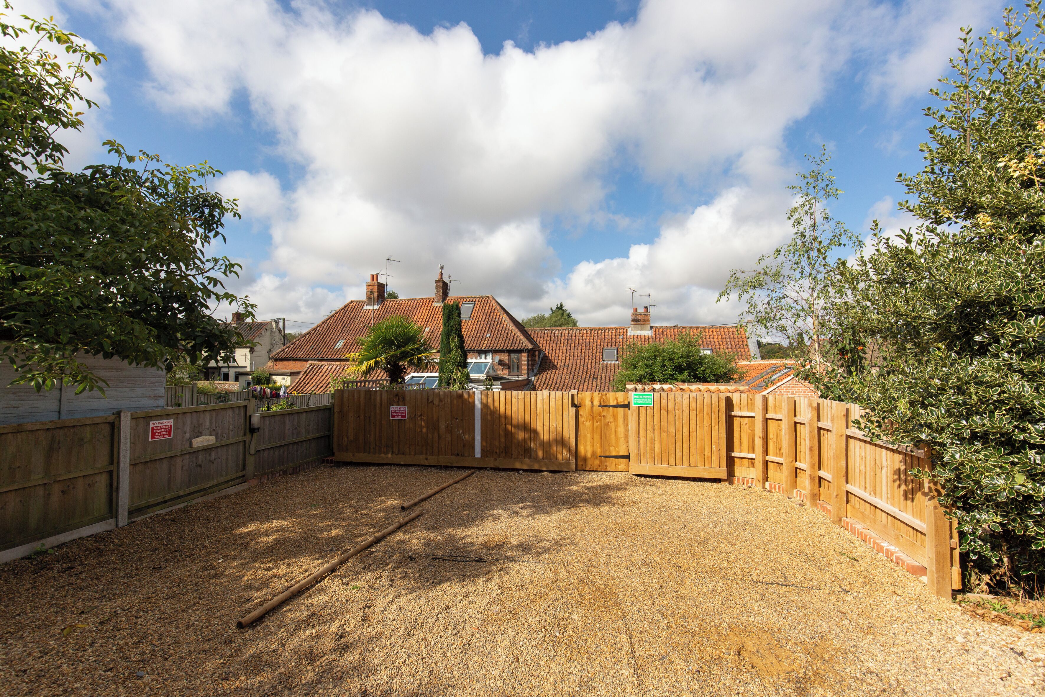 A fenced outdoor area with a gravel ground, wooden fence, and a building with a tiled roof in the background.