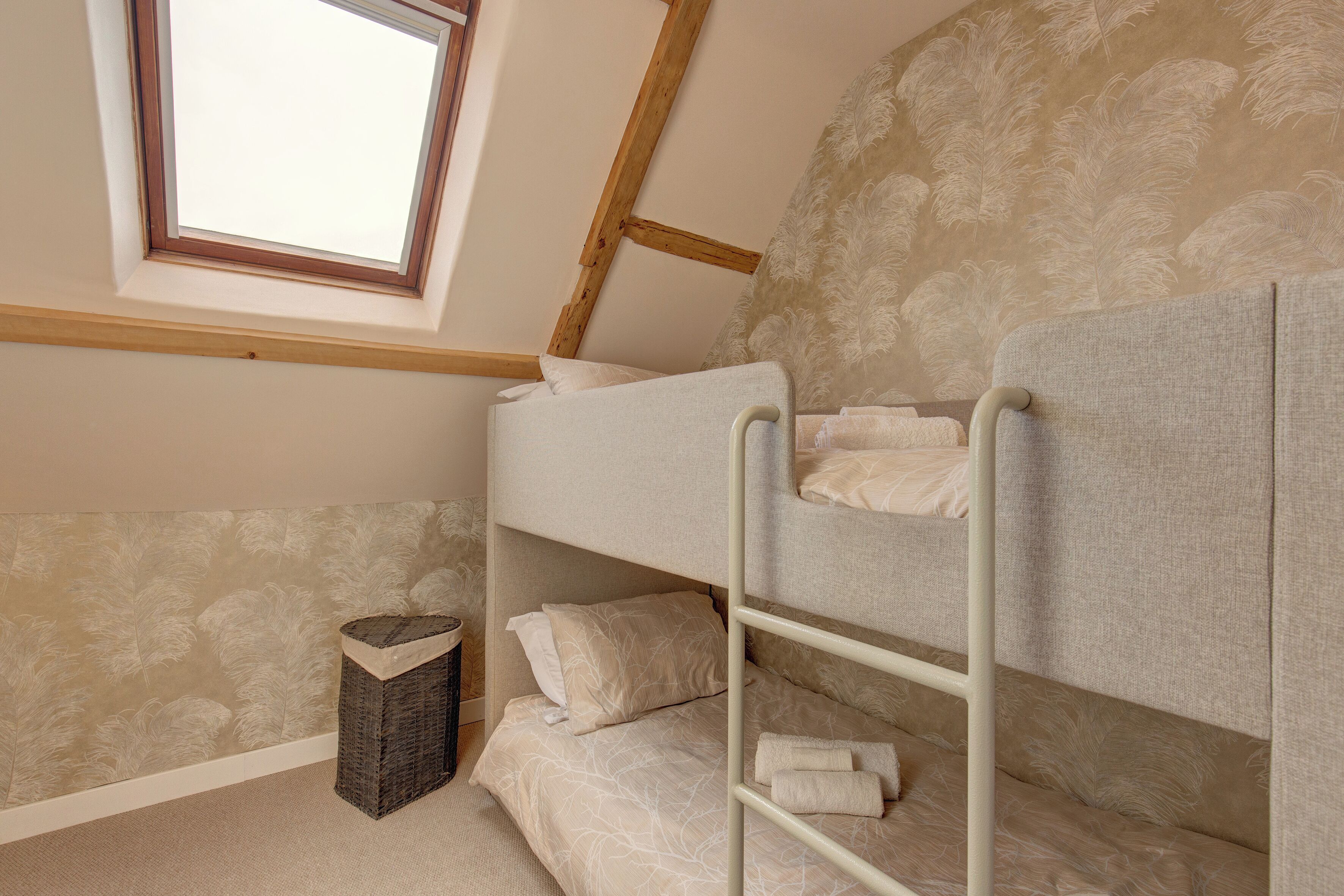 A bunk bed room with a skylight, patterned wallpaper, and a small trash bin.
