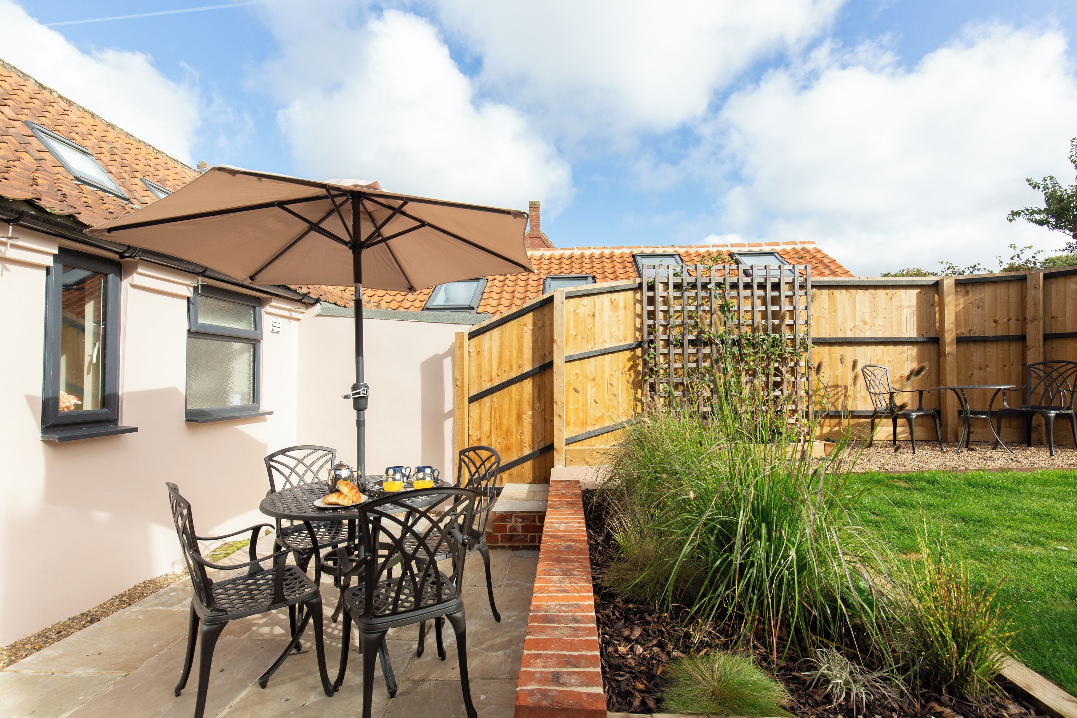 Une terrasse avec une table et des chaises, une clôture en bois et une cour gazonnée.