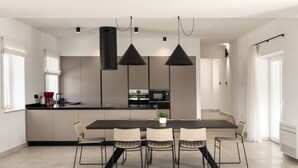 Una cocina moderna con una isla central, iluminación colgante y un comedor con sillas.