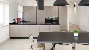 Una cocina moderna con una isla central, un comedor con mesa oscura y una escalera que lleva a otro nivel.