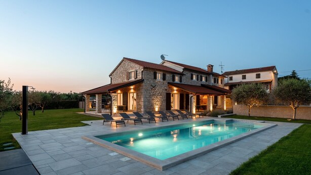 Una amplia casa de piedra con piscina, mobiliario exterior y un césped bien cuidado.