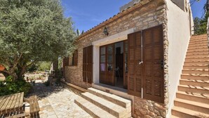 Un bâtiment en pierre avec des volets en bois, un escalier en pierre et un banc en bois.