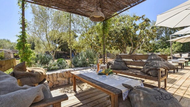 Une terrasse extérieure avec des meubles en bois, un plafond en osier et des murs en pierre.