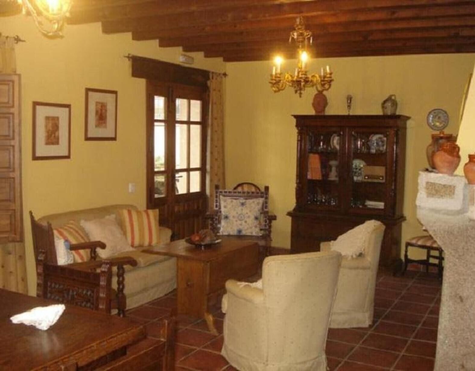 A cozy living room with a wooden sofa, armchairs, a coffee table, and a cabinet with glass doors.
