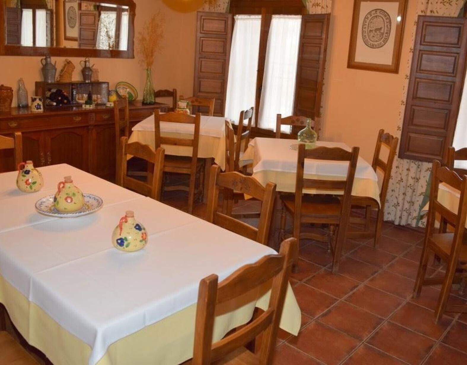 Un espace repas avec des tables et des chaises en bois, un coin cuisine avec des placards et un évier, et un sol carrelé.