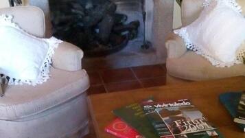 Un salon avec deux fauteuils, une table basse avec des magazines et une cheminée.