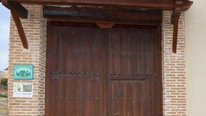 Una puerta de madera grande con un cierre metálico, flanqueada por muros de ladrillo y dos pilares de piedra.