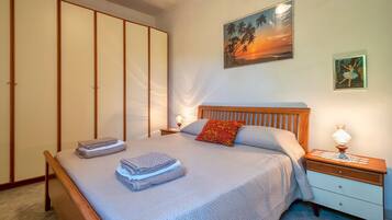 Una cama bien tendida con toallas dobladas, un cabecero de madera, una mesita de noche con lámpara y un cuadro de una puesta de sol.