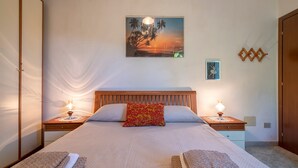 Ein ordentlich bezogenes Bett mit Kissen, Nachttischlampen, einem Wandbild und einem Holz-Kopfende.
