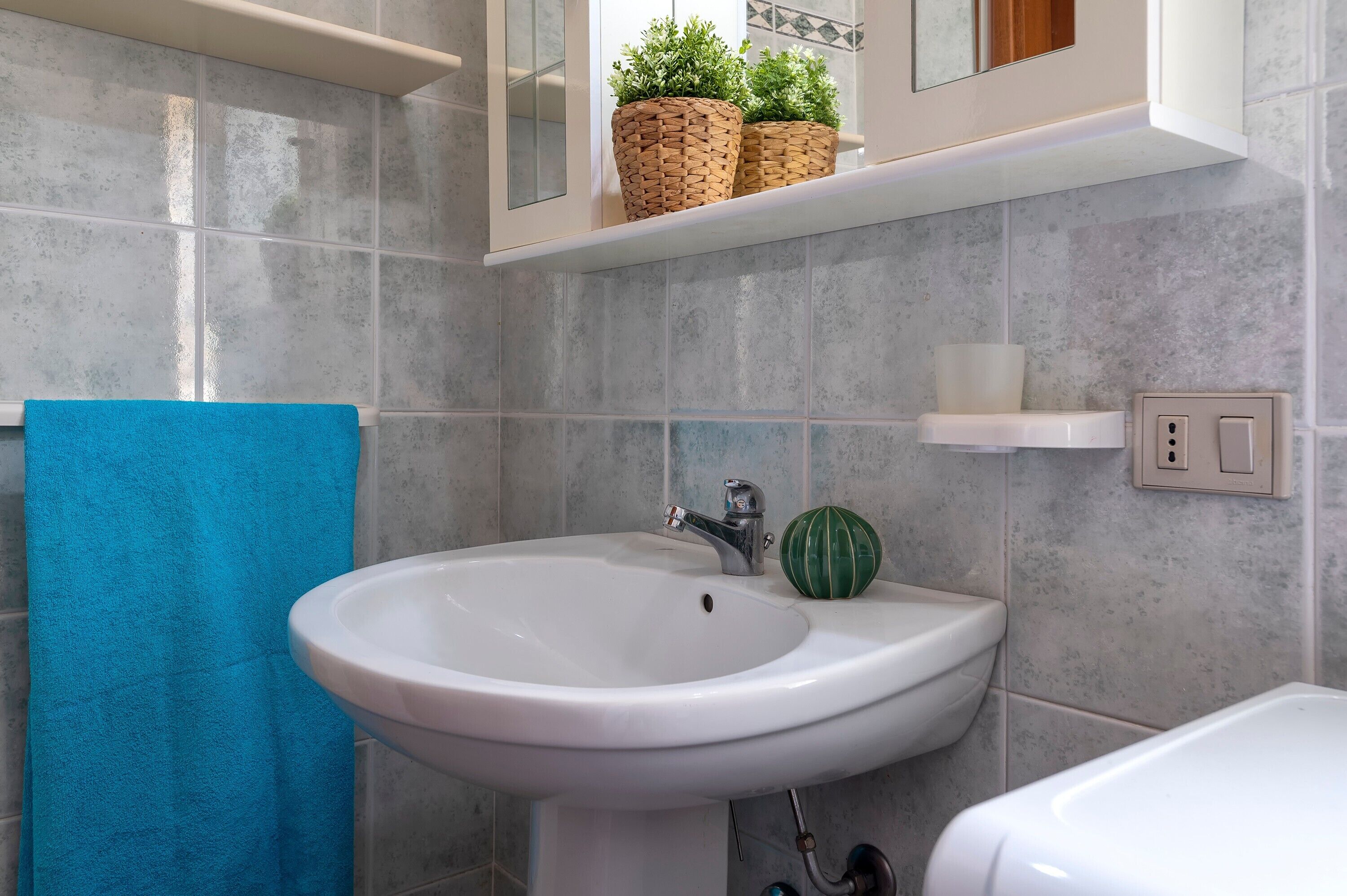 Ein Badezimmer mit einem weißen Waschbecken, einem blauen Handtuch und einem grünen Wanddekor.