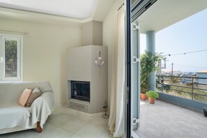 Een woonkamer met een bank, open haard en balkon met plantenpotten.