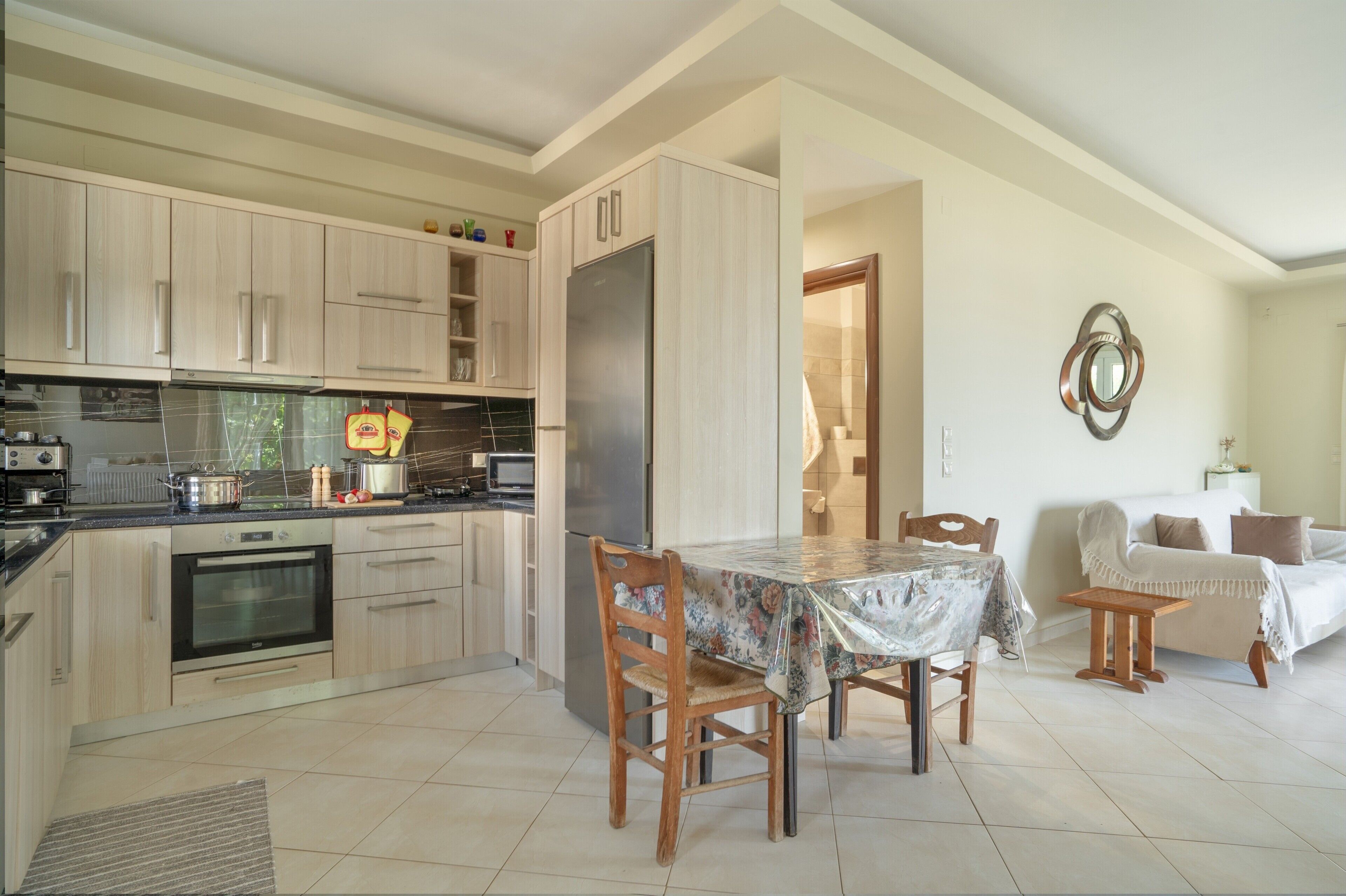 Une cuisine moderne avec des meubles en bois, une table à manger avec des chaises et un coin salon avec un canapé et une petite table.