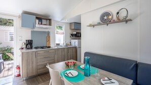 A compact kitchen with modern appliances, a dining area with a bench, and a small seating area. - Mobile Home on Family Campsite with Pools (Saint-Jean-de-Monts)