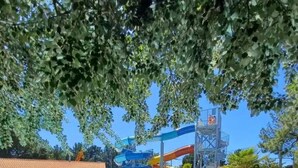 A swimming pool with a water slide, surrounded by trees and a building with a tiled roof. - Mobile Home on Family Campsite with Pools (Saint-Jean-de-Monts)