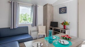 A modern room with a sofa, a dining table with glasses and plates, a TV, and a potted plant. - Mobile Home on Family Campsite with Pools (Saint-Jean-de-Monts)