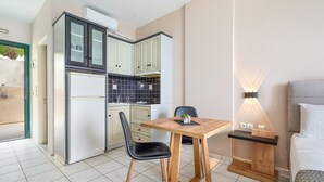 A compact kitchen with a dining table, chairs, and a small bedside table with a lamp.