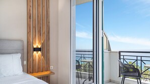 A bedroom with a bed, a wooden wall panel, a nightstand, a window, and a balcony with a table and chairs.
