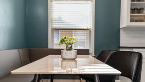 A dining area with a table, chairs, a vase with a plant, and a window with blinds.