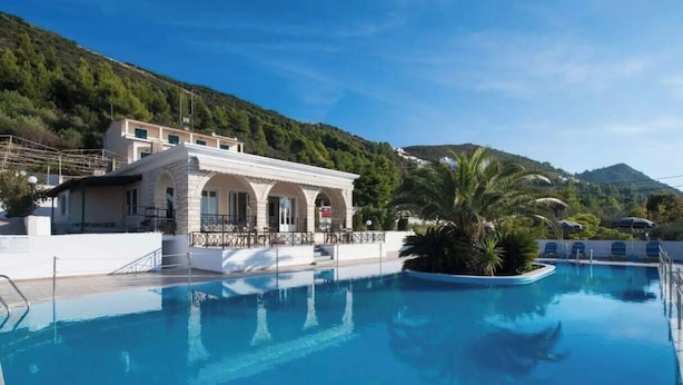 A swimming pool with a building in the background, surrounded by greenery and hills. - Studio Apartment 'Sunset Premium  11' with Sea View, Wi-Fi and Air Conditioning (Lefkada)