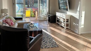 A living room with a sofa, coffee table, TV, and a balcony with outdoor furniture.