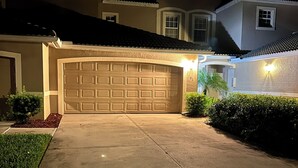 A residential driveway leading to a garage with a lighted exterior wall.