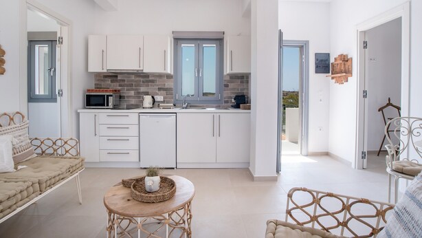 Une cuisine moderne avec des meubles blancs, un four à micro-ondes et un évier. On y trouve également un coin repas avec une table et des chaises en osier.